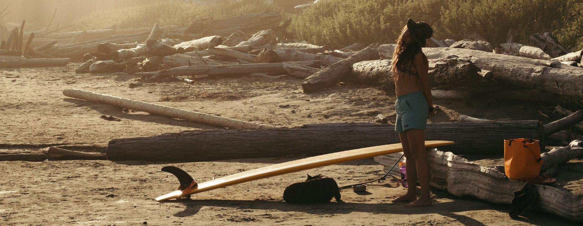 Woman with a RUX Waterproof Bag and a surfboard at the beach in Tofino, BC